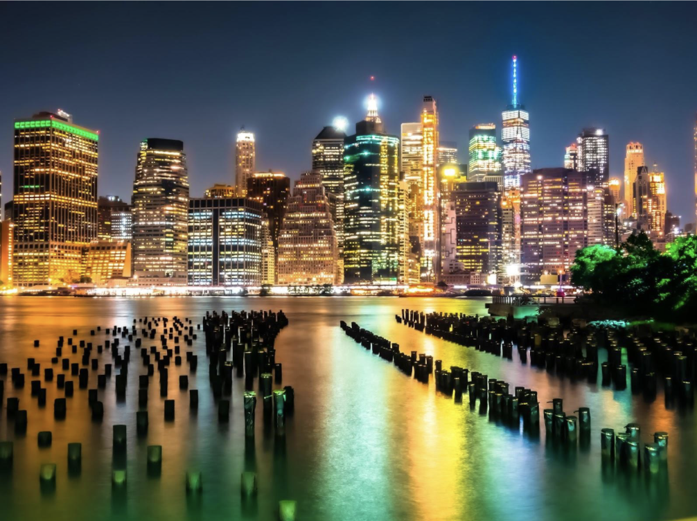 The bright New York City skyline reflects off of water.